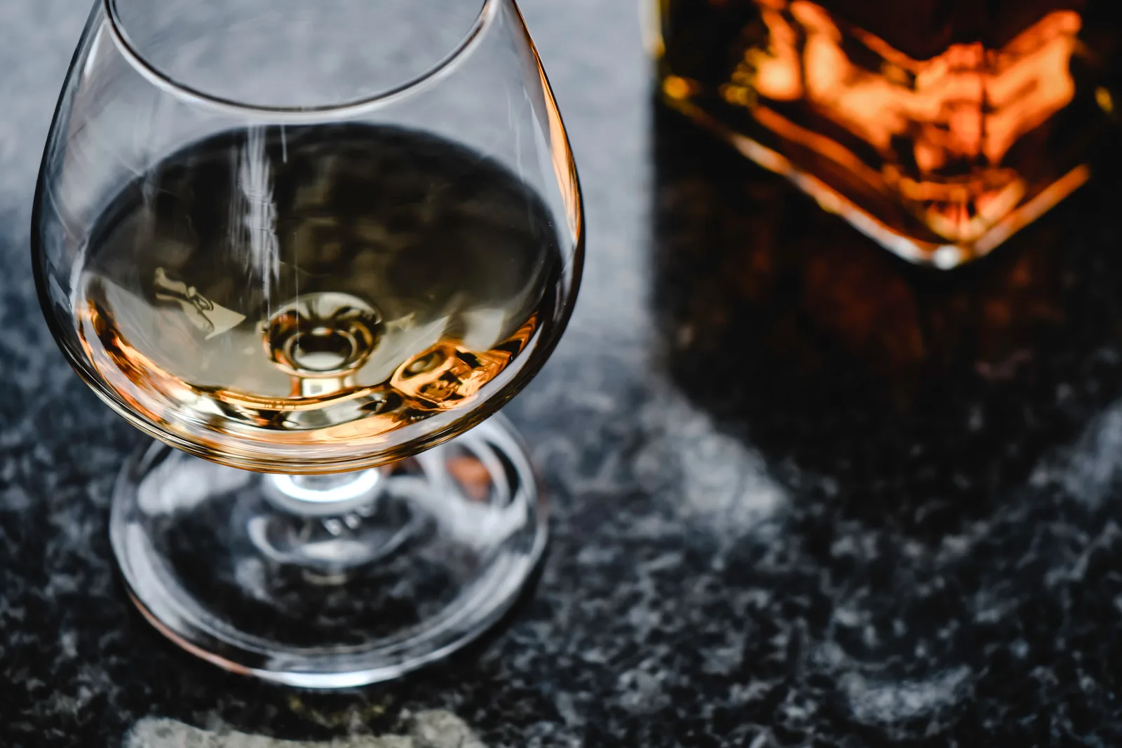 Bernsteinfarbene Cognac-Flüssigkeit in einem Schwenkglas, dahinter ein Eichenfass als Symbol für die Duftnote Cognac