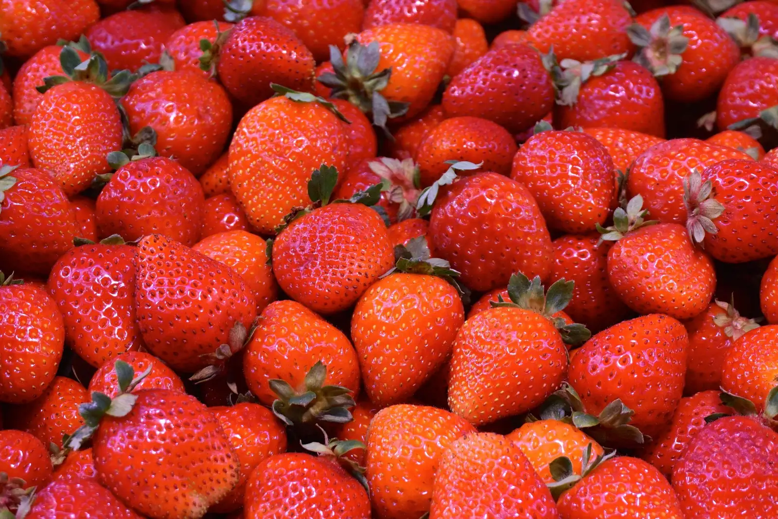 Reife rote Erdbeeren mit grünem Kelchblatt, im Hintergrund ein Parfümflakon in warmem Licht