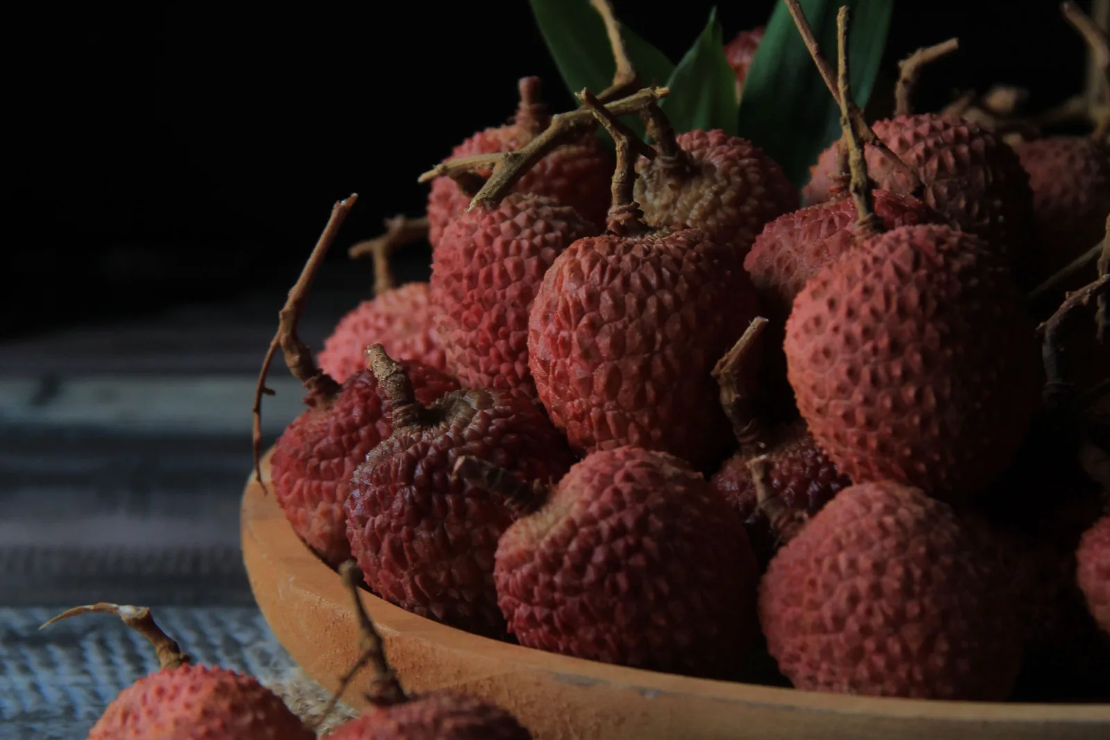 Aufgeschnittene, rosafarbene Litschi-Frucht mit glänzendem, durchscheinendem Fruchtfleisch neben Rosenblüten