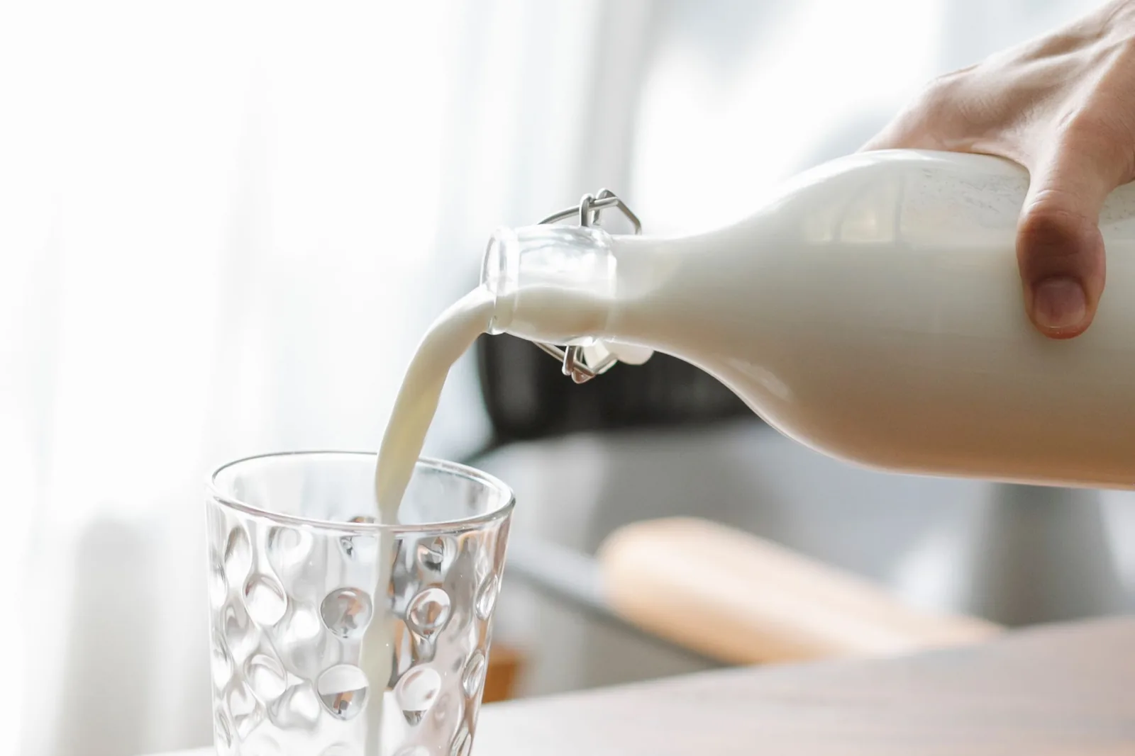 Ein Glas Milch neben aufgeschnittener Vanilleschote und Kokosraspeln auf heller Holzoberfläche
