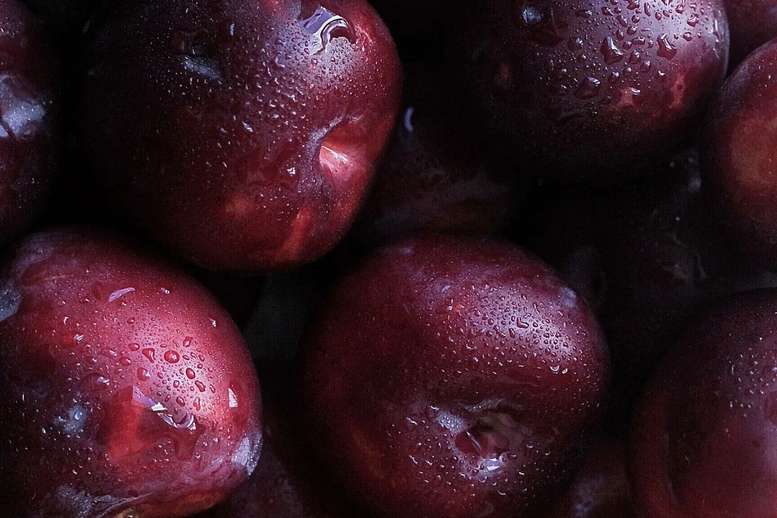 Reife dunkelviolette Pflaumen, halb aufgeschnitten, mit Duftöl-Fläschchen