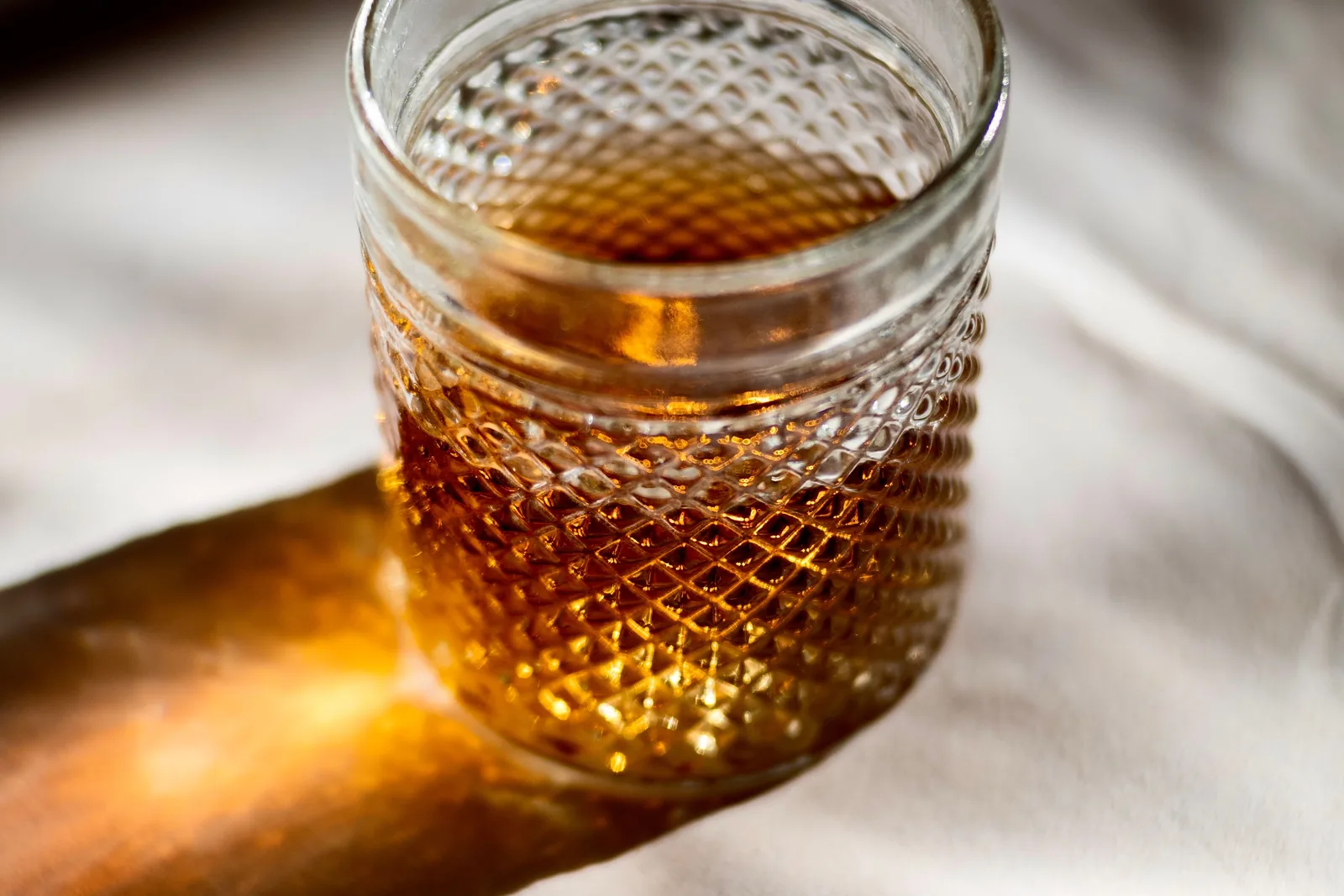 Bernsteinfarbener Rum in einem Glas neben Vanilleschoten und brauner Zuckermasse auf dunklem Holz