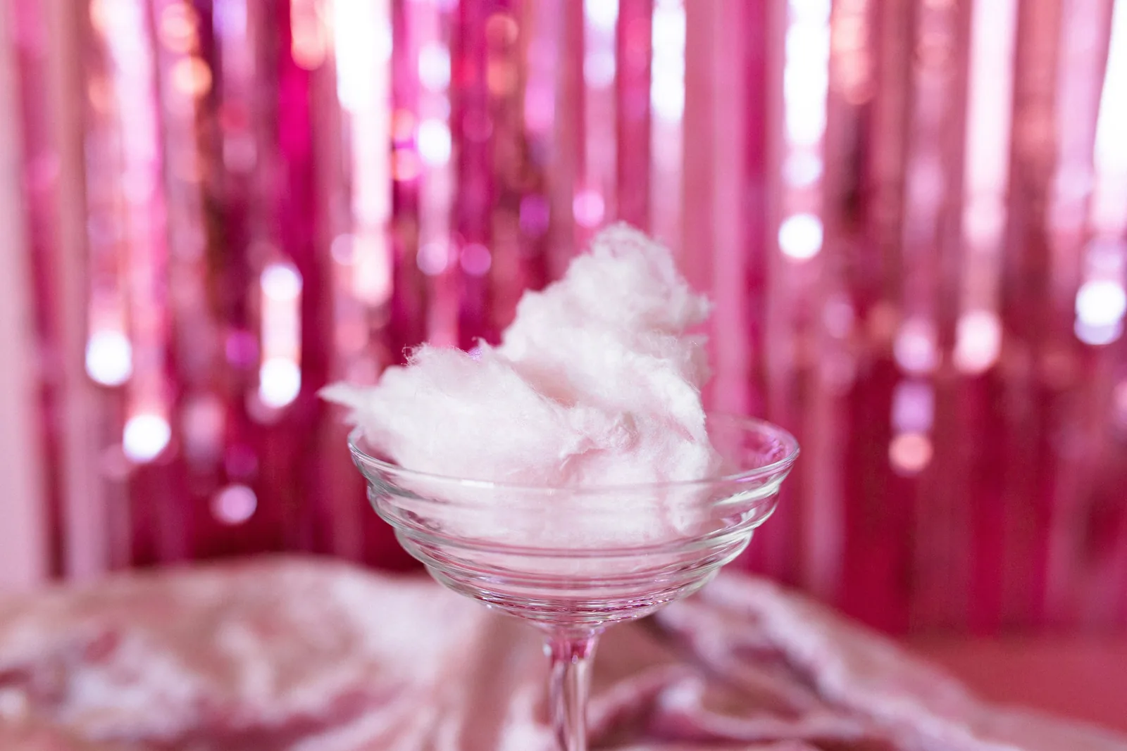Rosa Zuckerwatte auf Papierkegel neben Parfümflakon mit Karamellton