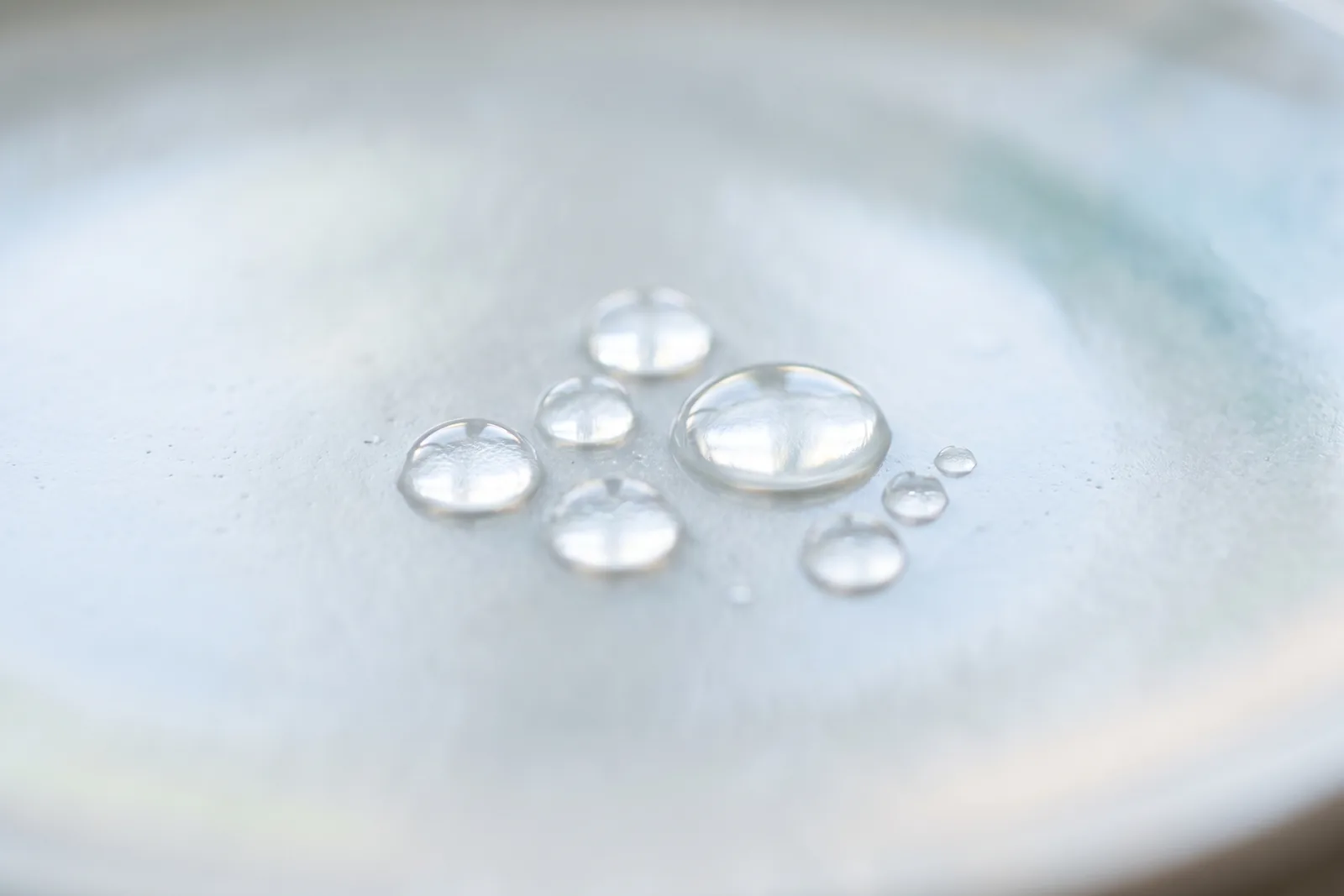 Klare Wassertropfen auf einer glatten hellen Oberfläche im Tageslicht als Sinnbild für frische Duftrichtungen