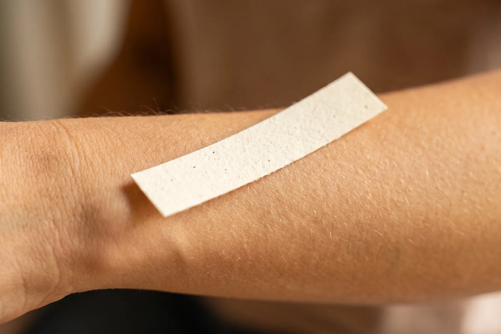 Ein Teststreifen neben einem Handgelenk in neutralem Licht als Bild für den Vergleich zwischen Papier- und Hauttest